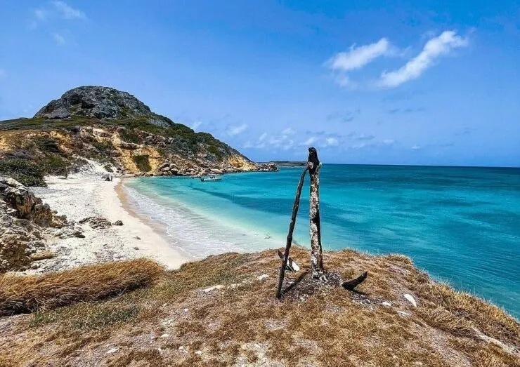 Old anchor set on a rocky rise above a white-sand beach on Caja de Muertos