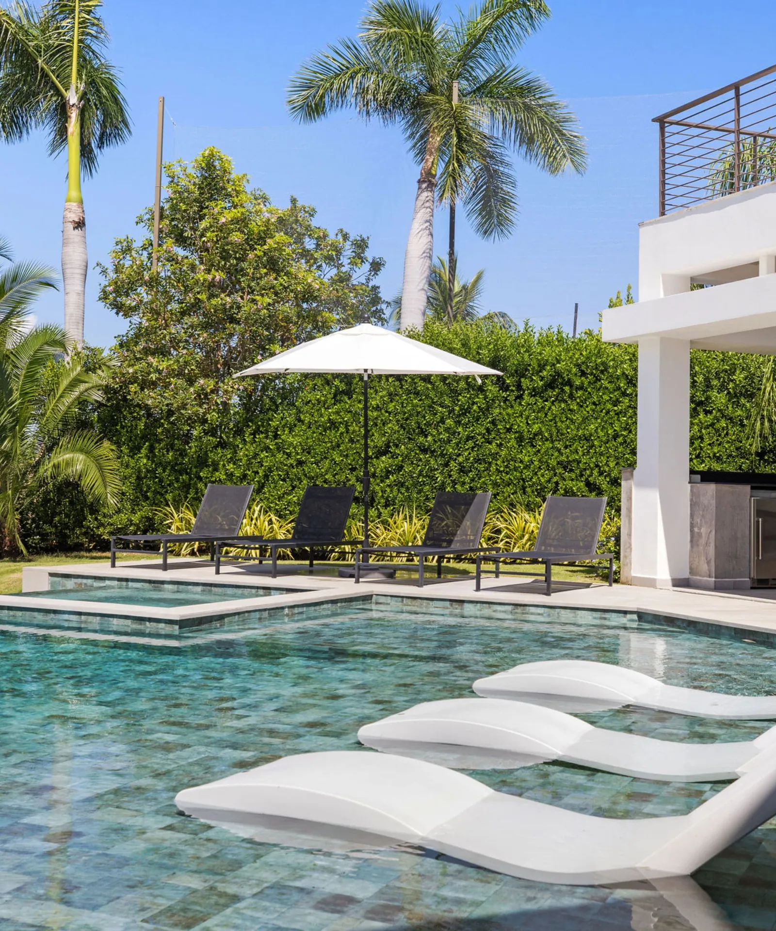 Pool with in-water loungers and palm trees next to a modern home