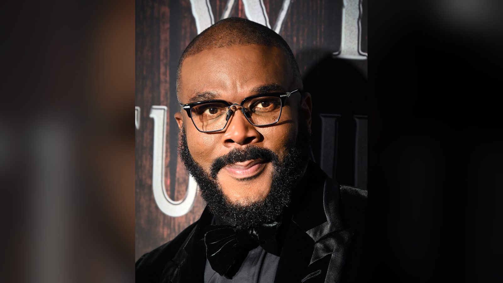Tyler Perry, sonriente, con gafas y esmoquin de terciopelo negro con corbatín, en un estreno de Broadway en abril de 2026.