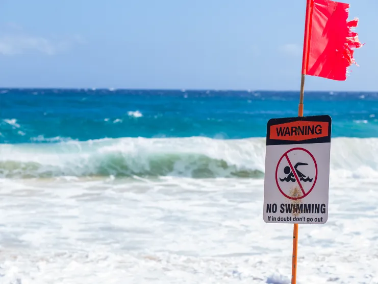 Bandera roja y letrero que prohíbe nadar en una playa con oleaje