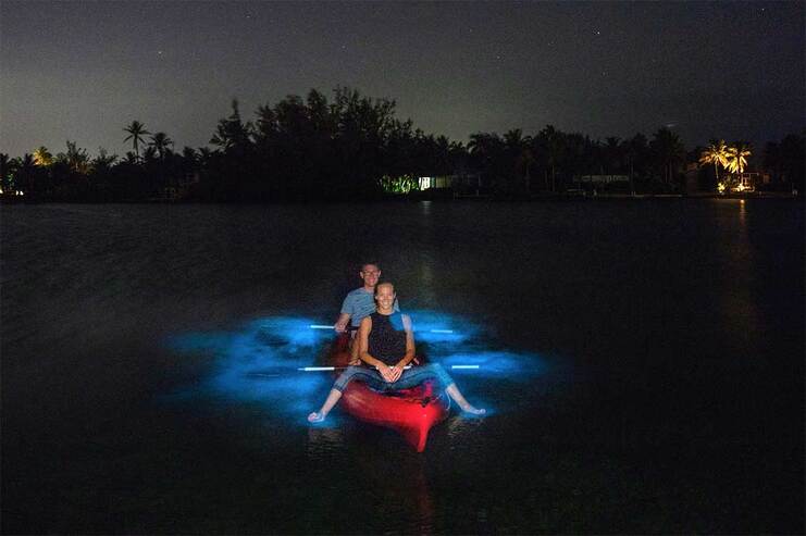 image of two people in a kayak in the water with bioluminescence glowing around them